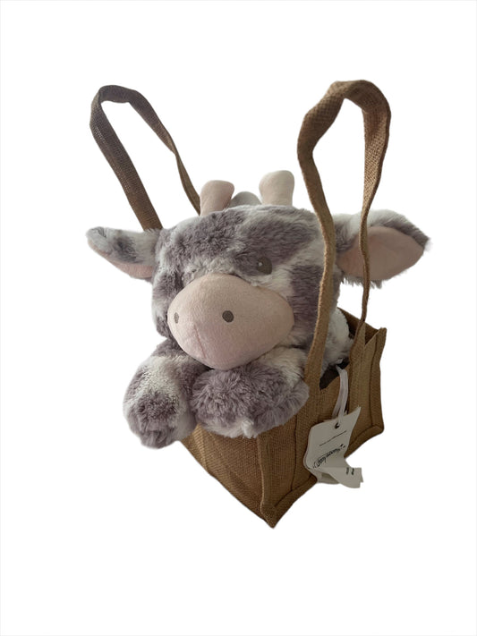 Cheeky cow look-alike with patchy top deck/caramilk coloured, fluffy plush giraffe head resting adorably on its paws, sitting propped up in a natural, brown hessian jute bag